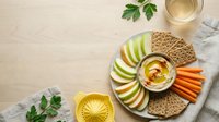 Healthy snack platter with hummus, fresh vegetables, apple slices and crackers on wooden background for nutritious eating and appetizer presentation.