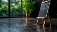 Empty wooden easel with small blackboard standing on reflective dark floor in room with green plants and natural lighting through windows. For education concepts.