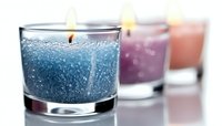 Glowing scented candles in glass holders with blue, purple and pink gel wax creating atmospheric mood lighting with bokeh effect and shallow depth of field.