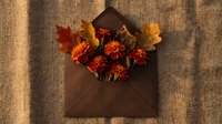 Autumn envelope with orange flowers and colorful fall leaves on rustic burlap background, flat lay composition for seasonal greeting cards.