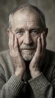 Thoughtful senior Caucasian man with gray beard resting face in hands, expressing contemplation and wisdom in warm indoor portrait for aging concepts.