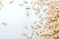Raw white rice grains scattered on white background, creating minimalist food composition with copy space for culinary or agricultural concepts.