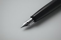 Close-up view of fountain pen nib on gray background showing detailed metalwork and writing tip, minimalist composition suitable for business and education concepts.