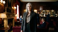 Professional middle-aged Caucasian businesswoman in elegant suit standing confidently in upscale hotel lobby or bar with warm lighting and luxury interior.