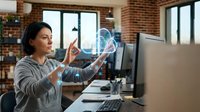 Young Hispanic businesswoman using holographic technology interface at modern office workspace with brick walls and computer setup.