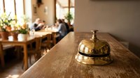 Vintage brass service bell on wooden hotel reception desk in warm lobby interior with blurred background for hospitality and customer service concepts.
