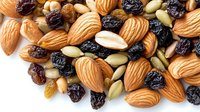 Mixed nuts and dried fruits scattered on white background, including raw almonds, raisins, pumpkin seeds and other nutritious snacks for healthy eating.