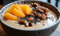 Creamy smoothie bowl topped with fresh mango slices, crunchy almonds and black chia seeds in ceramic bowl, healthy breakfast concept for clean eating.