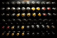 Wine bottles stored in traditional wooden rack, view from above showing cork ends. Dark cellar atmosphere with dramatic lighting highlighting red and white varieties.