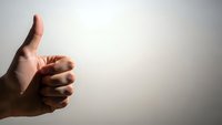 Hand showing thumbs up gesture against neutral background expressing approval, success, positive feedback and satisfaction for business concepts.