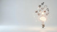 Glowing light bulb with business icons floating above on white background representing innovation and creative ideas for marketing campaigns.