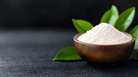 Pink Himalayan salt in wooden bowl with fresh green leaves on dark background, selective focus. Natural spa and wellness concept for healthy lifestyle.
