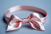 Elegant pink satin bow headband with delicate stitching detail on soft blue background, showcasing feminine accessory for special occasions and fashion styling.