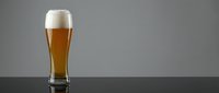 Fresh golden beer with white foam head in tall glass on dark surface against gray background for beverage advertising and bar promotions.