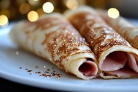 Thin crepes rolled with ham filling and dusted with cocoa powder on white plate, soft bokeh lights in background create cozy atmosphere for breakfast or brunch.