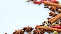 Aromatic Christmas spices including cinnamon sticks, star anise, cloves and cardamom pods arranged on white background for holiday baking and cooking.