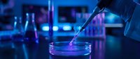 Scientist pipetting blue liquid into petri dish in laboratory with glowing equipment and data charts, representing biotechnology research and scientific innovation.