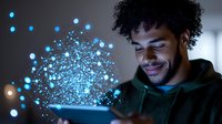 Young African American man in green hoodie smiling while using tablet device with glowing blue particles emerging from screen, representing digital transformation and technology.