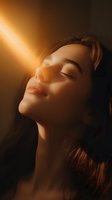 Young Asian woman with closed eyes in warm sunlight, face tilted up with serene expression against dark background, dramatic side lighting creates ethereal mood.