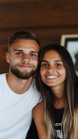 Young interracial couple smiling at camera, close-up portrait. Caucasian man with beard and Hispanic woman with nose piercing wearing casual attire against wooden background.