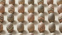 Decorative Easter eggs with intricate geometric patterns in neutral brown tones arranged on soft fabric background for spring holiday celebrations.