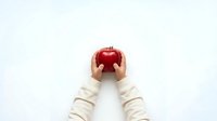 Hands in cream sweater holding fresh red apple on white background, isolated for design use on merchandise and promotional materials.