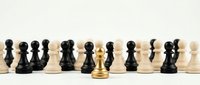 Golden chess king piece standing out among black and white pawns on wooden board representing leadership, strategy and business success concepts.