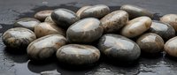 Smooth river stones scattered on wet dark slate surface with water droplets creating natural spa and zen meditation atmosphere for wellness design.