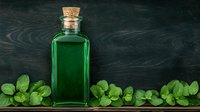 Green glass bottle with cork stopper on dark wooden background decorated with fresh mint leaves, suitable for wellness, spa and aromatherapy concepts.