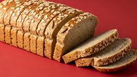 Sliced whole grain bread loaf with seeds and nuts on red background. Healthy artisan bakery product for breakfast, sandwiches and nutritious meals.