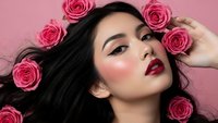 Young Asian woman with dark hair surrounded by pink roses on pink background for beauty and cosmetics advertising campaigns.