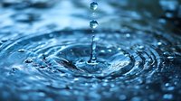 Water drops falling into blue rippling water surface creating concentric circles and splash with suspended droplets captured in macro photography.