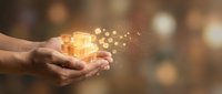 Hands holding glowing gift box with magical sparkles and warm bokeh lights creating festive holiday atmosphere for celebration and giving concepts.