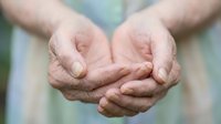 Elderly hands cupped together in protective gesture showing care, support and offering help. Wrinkled skin texture reveals age and life experience in compassionate pose.