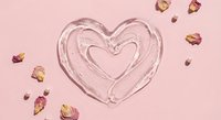 Glass heart shape with dried rose petals on pink background for romantic Valentine's Day wedding anniversary love celebration greeting card design.