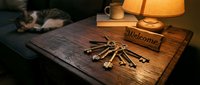 Rustic wooden table with a bunch of vintage keys, a welcome sign, warm lamp light, and a sleeping cat in a cozy home interior.