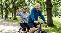 Happy senior couple riding bicycles together in sunny park, elderly man and woman enjoying active lifestyle and outdoor recreation.