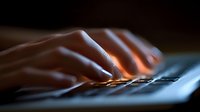 Fingers typing on keyboard in dark room with dramatic lighting, close-up view shows hands working on computer at night, creating moody atmosphere for business concept.
