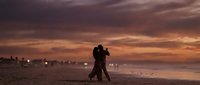 Romantic couple dancing on beach at sunset with dramatic orange and purple sky reflecting on wet sand creating intimate silhouette moment for love and relationship concepts.