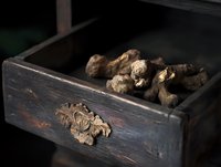 Dried ginger root pieces in vintage dark wooden drawer with ornate carving detail, moody natural lighting creates dramatic shadows and rustic atmosphere.
