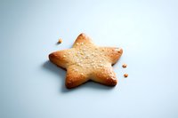 Star-shaped butter cookie with golden brown edges and crumbs on light blue background, isolated for easy design integration in food and holiday projects.