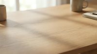 Clean wooden desk surface with natural grain texture and warm lighting creating soft shadows in modern workspace environment.