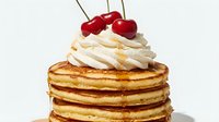 Stack of golden pancakes topped with whipped cream and fresh red cherries on white background. Breakfast dessert food isolated for menu design.
