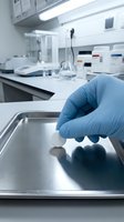 Scientist wearing blue latex glove holding sample in modern laboratory with equipment and instruments on workbench for research and analysis.