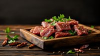 Raw beef chunks seasoned with spices and herbs on rustic wooden serving board against dark background, garnished with fresh parsley and chili peppers.