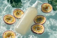 White cosmetic bottle with fresh passion fruit slices floating in splashing water on green background, natural skincare product photography for beauty industry.