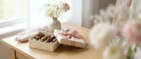 Elegant gift box with chocolates and fresh flowers on wooden table near window, perfect for celebrations, holidays, and special occasions.