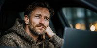 Thoughtful middle-aged Caucasian man with beard in cozy sweater looking contemplative while sitting indoors with warm lighting and bokeh background.