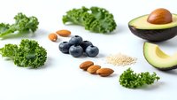Fresh superfood ingredients including kale, avocado, blueberries, almonds and quinoa arranged on white background for healthy eating and nutrition.