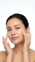 Young Asian woman applying facial moisturizer cream with hands on white background for skincare beauty routine and cosmetic product advertising.